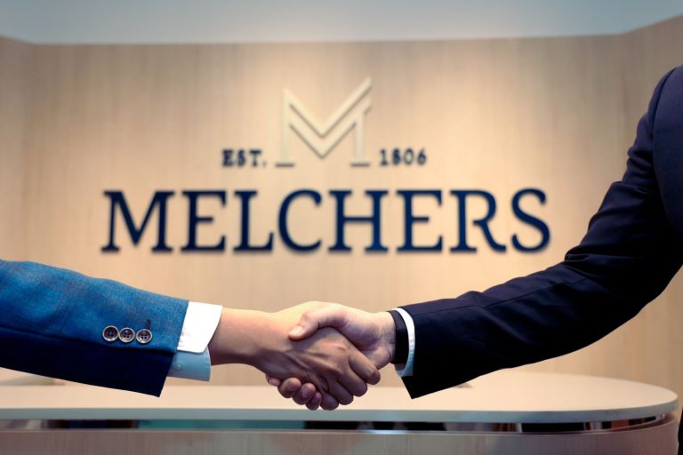 Handshake between two people in suits with the Melchers logo in the background