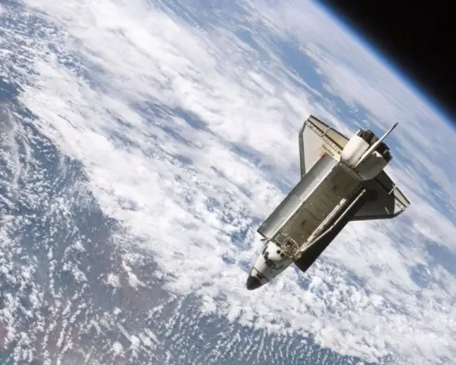 Ein Space Shuttle umkreist die Erde, wobei die Erdoberfläche und die Wolken vor dem schwarzen Hintergrund des Weltraums zu sehen sind.