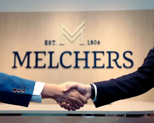Händedruck zwischen zwei Personen in Anzügen, im Hintergrund ist das Melchers‑Logo zu sehen.
